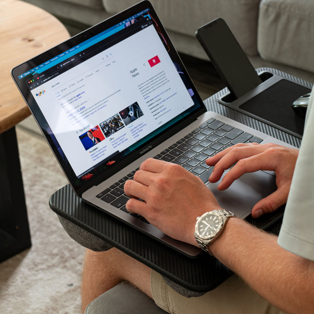 Black Carbon Home Office Lap Desk is used by the model while he works on his laptop. He also has his phone in the phone holder and has a mouse on the mouse pad that is built into the lap desk.